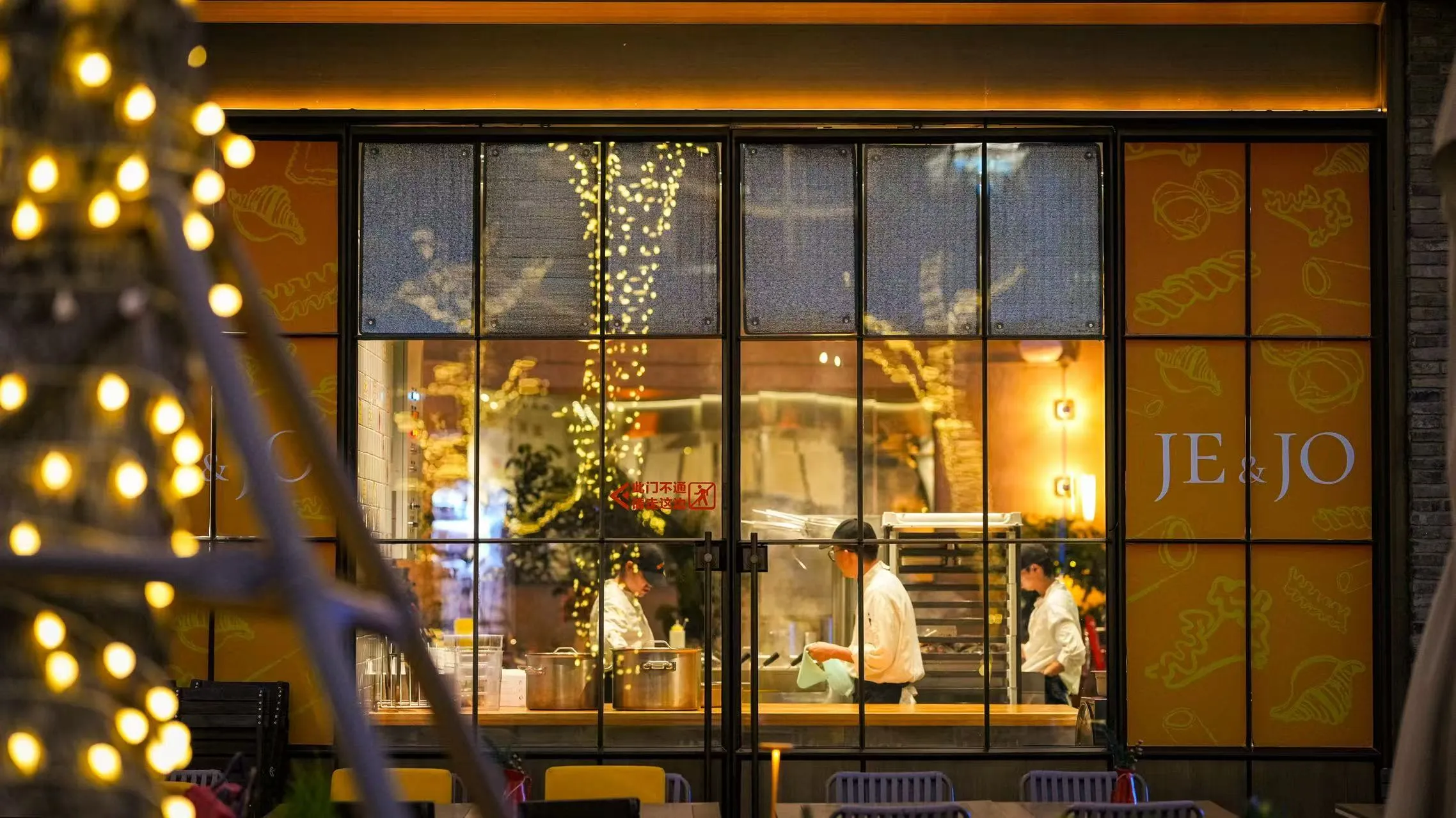 夜晚的 JE&JO 店面，透过玻璃可见厨师在明档内忙碌