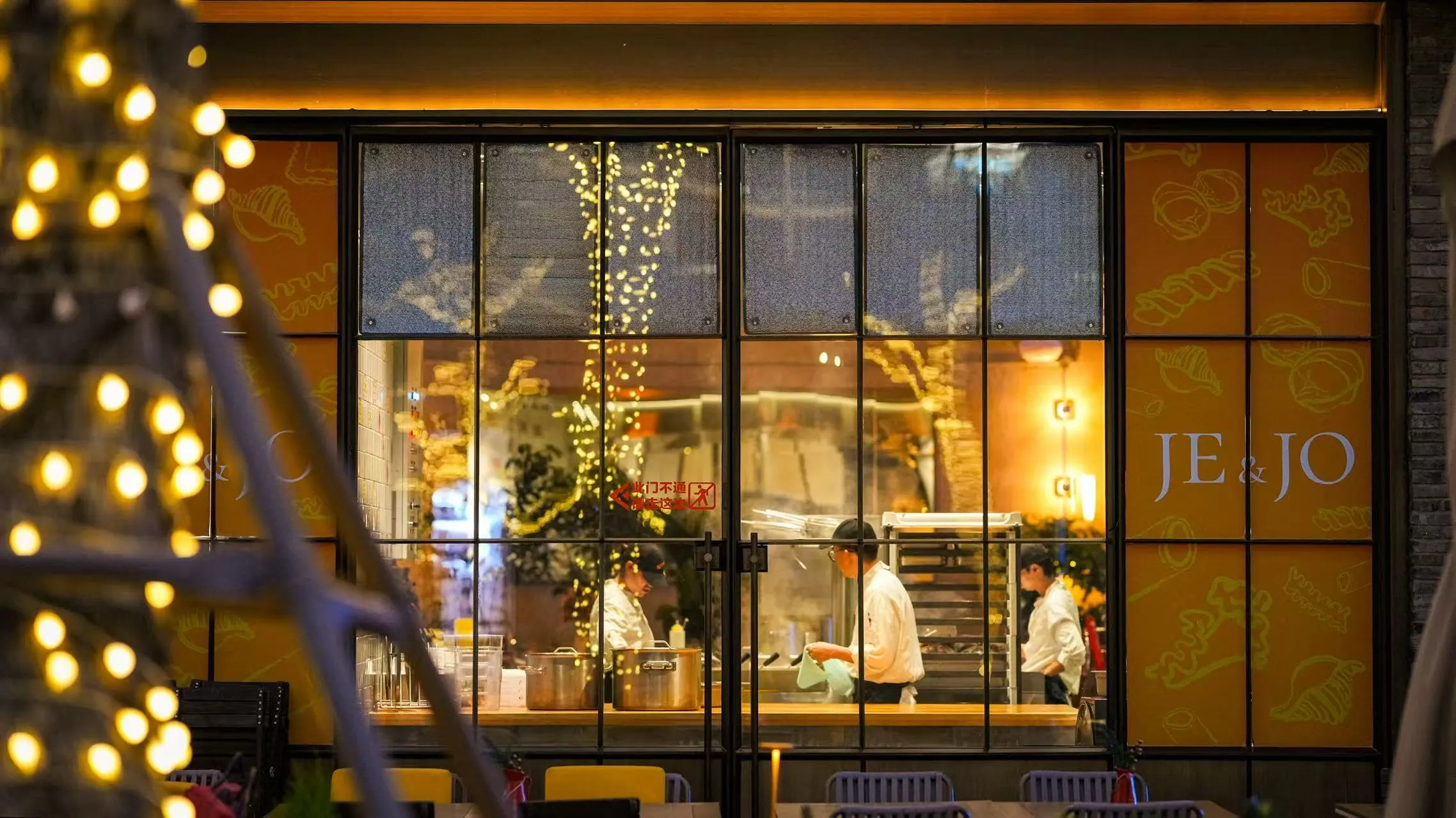 夜晚的 JE&JO 店面，透过玻璃可见厨师在明档内忙碌