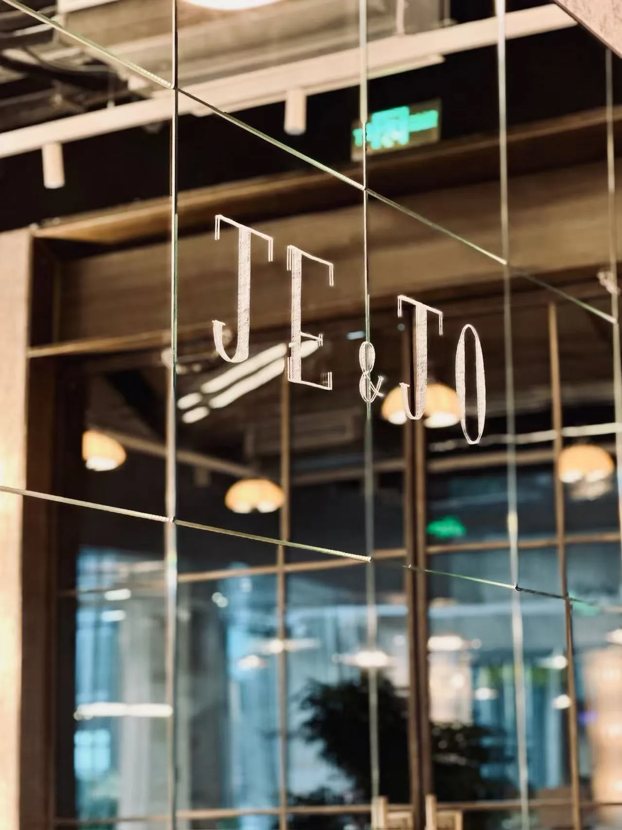 玻璃上蚀刻的 JE&JO 店名，背景是暖色灯光的用餐区